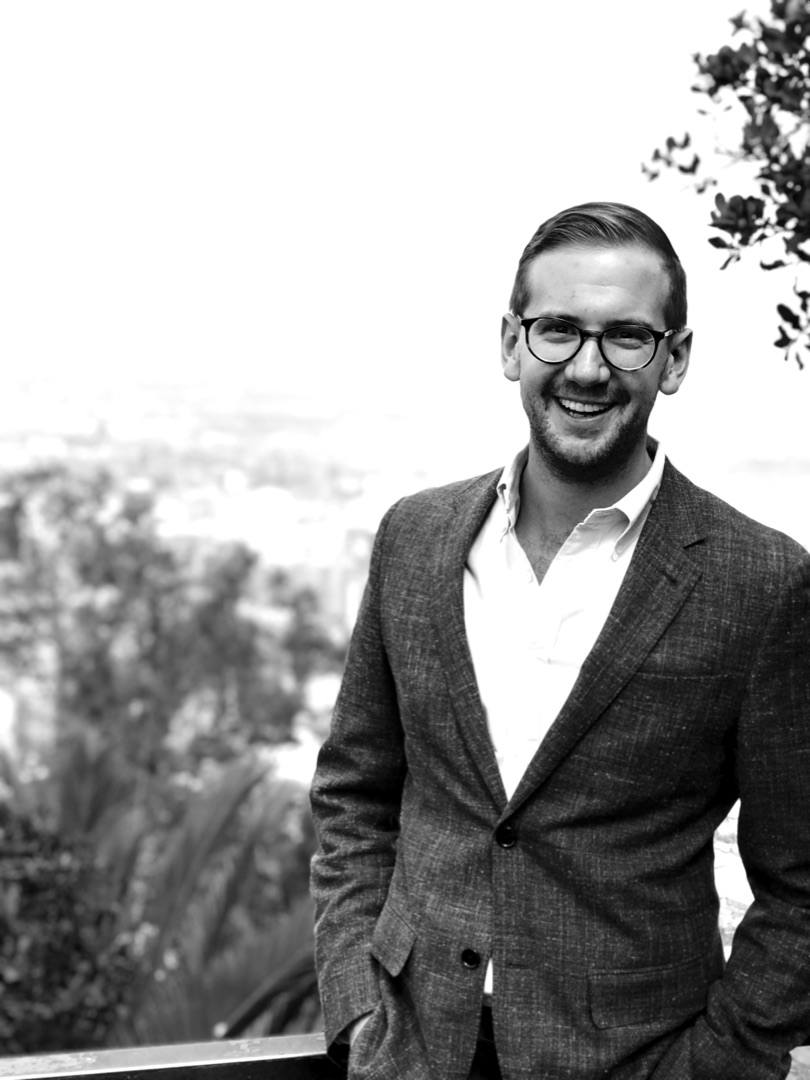 James Costantini, smiling, wearing glasses and a blazer